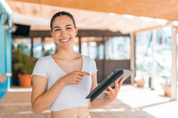 Young pretty woman at outdoors touching the tablet screen with happy expression