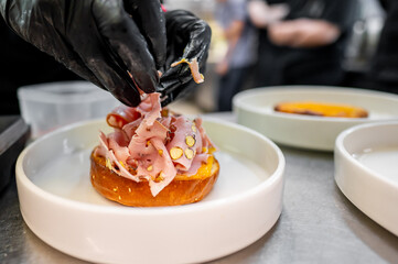 A chef’s gloved hands adding toppings to an open-faced sandwich in a professional kitchen