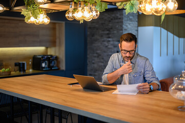 Serious financial advisor reading and auditing report while working at desk in illuminated office