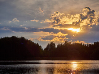 Evening landscape. Sunset sun in the clouds and dark silhouette of the forest
