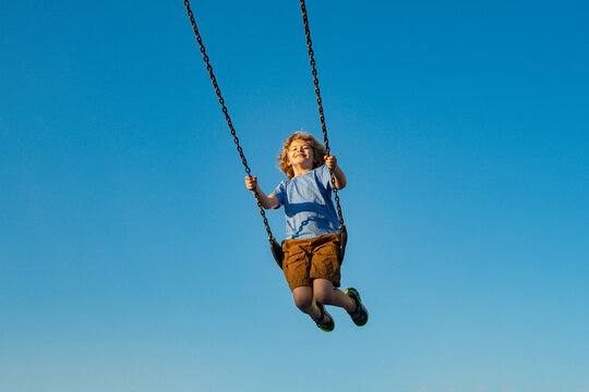Naklejki Child extreme swinging. Danger high Swing in sky. Swing fly. Cute child having fun on a swing on summer sky background. Kids playing in park. Blonde little boy swings at kid playground.