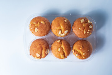 Freshly baked almond muffins in a transparent plastic tray on a white background.