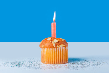 Birthday cupcake with glowing candles on white table with blue background. Closeup