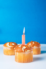 Birthday cupcakes with glowing candles on white table with blue background. Vertical shot