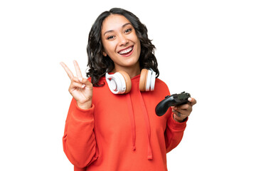 Young Argentinian woman playing with a video game controller over isolated background smiling and showing victory sign © luismolinero