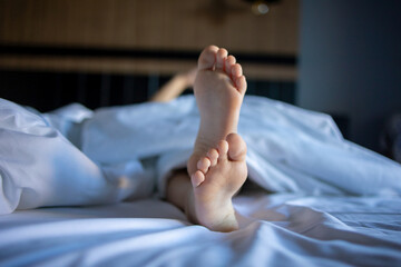 A frame that focuses on the sleeping legs of a baby sitting on a large white bed, reflecting the...