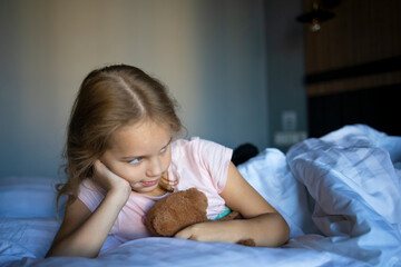 A pretty smiling blonde little girl in beautiful pajamas on a large and cozy bed after a night's...