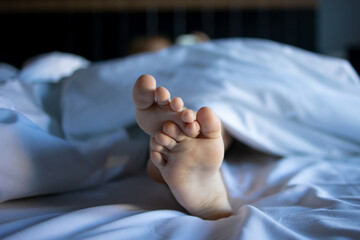 A close-up of the legs of a sleeping small child on a large white bed, embodying the concept of...