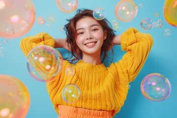 Cute happy young woman in a yellow sweater with colorful bubbles floating above her head isolated on a light turquoise background,