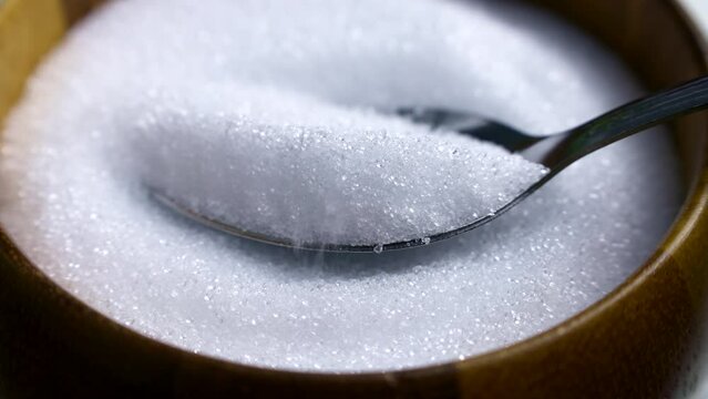 Spoon taking white natural organic sweet Erythritol sweetener granules from wooden bowl. Sugar substitute concept