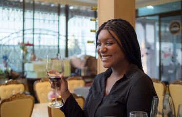 Portrait girl woman african one person celebrating smile happy enjoying people bar hand holding drink alcohol on glass wine and red wine bottle on dinner at party sitting in pub and restaurant cafe.