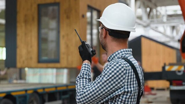 Foreman with walkie talkie manages the loading of a prefabricated modular house to truck
