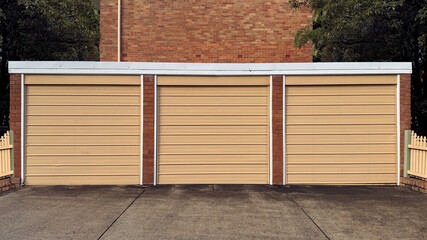 concrete driveway leading towards three cream color garage doors in a row on side of brick building