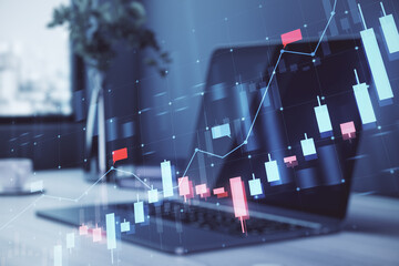 A laptop displaying stock market chart graphics with a holographic overlay concept on a modern office desk