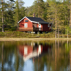 Obraz premium Off-grid, sun-powered, small traditional red wooden cabin by a small lake in Norway during the summer