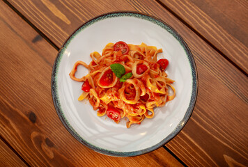 Pasta puttanesca with tomatoes, cooked food in spaghetti sauce, white plate on a wooden table.