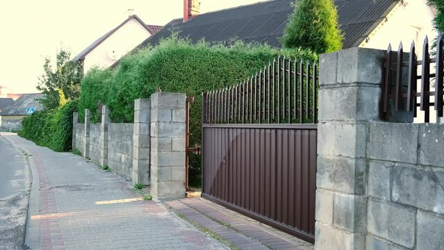 Opening of automatic entrance gate of brown color made of metal. Block fence. Entrance group for cars in the private house. Remote control. Smart home system