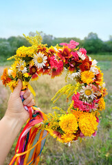 summer background. wreath of meadow flowers with colorful ribbons in hand outdoor. floral...
