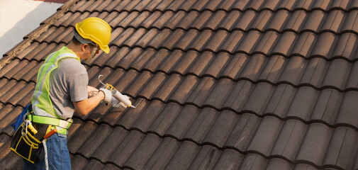 Worker man using silicone sealant adhesive  to fix crack of the old tile roof.