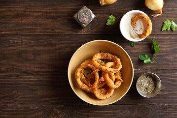 Crispy fried onion rings in bowl on wooden background