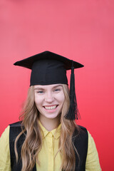 Young beautiful blond female in graduation cap with emotional facial expression on red background. Happy to finish school, college or university High quality photo