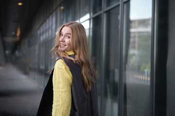 Beautiful blond female office worker on the background of office building . Positive emotions, wearing yellow shirt and jacket. High quality photo