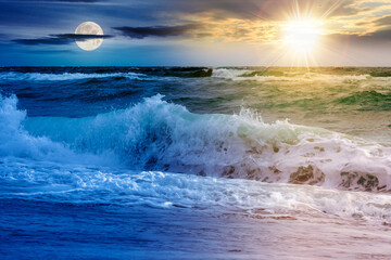 dramatic seascape at summer solstice. waves crashing the shore beneath a sky with sun and moon...