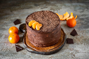 Sweet dessert: Chocolate cake with tangerines and chocolate cream on a wooden plate on a gray background.