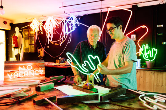 Standing men in neon signboard workshop checking product