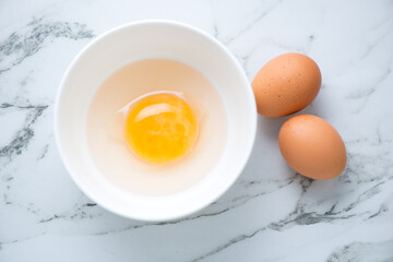 Bowl with uncooked goose and chicken eggs on a white marble background, horizontal shot, above view