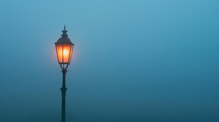 A single street lamp glows in the middle of a dense fog. The lamp is old-fashioned, with a black...