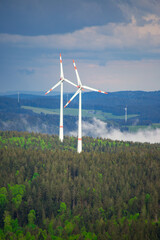 wind turbines in the mountain forest with a low fog under the trees