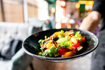 Close-up of a colorful dish with grilled vegetables and fresh herbs on a dark plate, suggesting an appetizing meal in an eatery