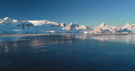 Polar frozen ocean landscape, ice on water surface. Snow covered mountain range, blue sky, sunny evening. Winter background. Breathtaking harmony of untouched nature. Scenery overview.