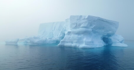 Giant iceberg drifts Antarctica ocean morning fog. Mystery dramatic mist scene. Glacier melting, climate change impact on polar environment. Antarctic travel and exploration. Drone shot close up