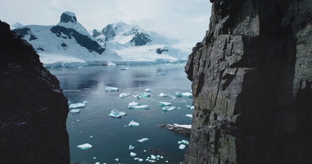 Aerial flight in mountain canyon Antarctica. Majestic snowy mountains towering polar ocean. Cracked glacier icebergs melting floating in cold ocean. Ecology, melting ice, climate change global warming