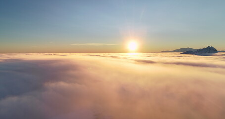 Mountain peak over sunset orange clouds sky. Tranquil scene morning sunrise fog sea overview. Sun shine over horizon, warm light texture. Nature background perfect landscape. Aerial panoramic flight