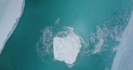 Aerial large iceberg floating blue ocean water in ice canyon. Snow covered glacier melting in...