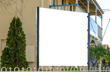 Blank white empty mockup background texture of a large, blank billboard over a metal fence in front of a residential building or a two-storey house. Copy space for design