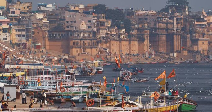 Varanasi, Uttar Pradesh, India. Many Boats are moored to the Ganga riverbank. Tourists boarding for an overnight boats ride on the Ganges River. Cityscape of Varanasi is visible - embankment in the