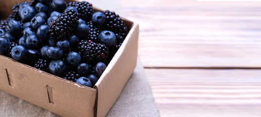 Fresh blackberries in a cardboard box on a wooden table with space for text