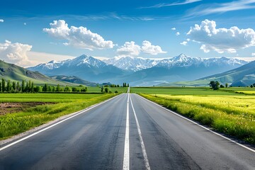 Naklejka premium A wide road leads into the distance, with green fields on both sides and snow-capped mountains in the background. The blue sky is clear, and white clouds float across it