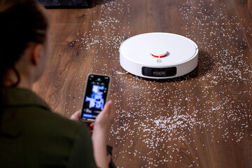 Woman using an app on his phone paired with a robotic cleaner. Display with apartment map, cleaning...