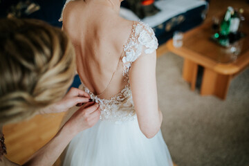 A bride or bridesmaid carefully adjusts the laces or buttons of a wedding dress, highlighting the...