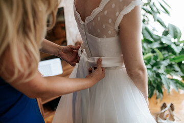 A bride or bridesmaid carefully adjusts the laces or buttons of a wedding dress, highlighting the detailed preparations and anticipation before the ceremony.