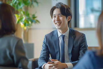 young Japanese business man having interview woman sitting his right side they talk smile while wearing suit modern office space atmosphere of their conversation friendly warm photo taken behind them