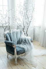 Luxurious blue velvet armchair with sheer white drapery, set amidst white decorative trees and soft, natural light. Perfect for promoting sophisticated home decor and elegant living spaces