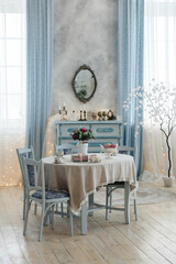 Beautifully decorated dining space featuring a vintage table with lace tablecloth, blue chairs, and floral centerpiece. Antique dresser and mirror enhance the room's elegant appeal