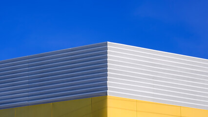 White corrugated steel with yellow aluminium composite tile wall on rooftop of industrial building against blue sky background in symmetric view, Geometric exterior architecture in minimal style