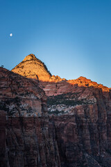 A breathtaking view of Zion Canyon Cliffs during sunrise with the moon overhead in Utah's Zion National Park. The early morning light casts a stunning glow on the rocky cliffs - USA